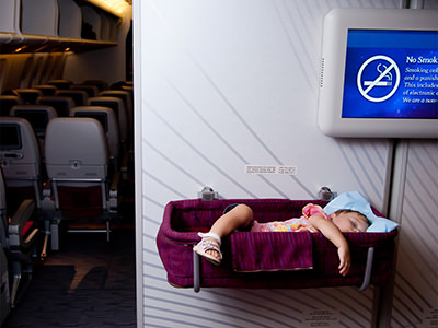 Two-year-old sleeping in a plane bassinet mounted on bulkhead wall, barely fitting in it, with arm and leg hanging out of it, photo by Nick Thompson, Depositphotos.com