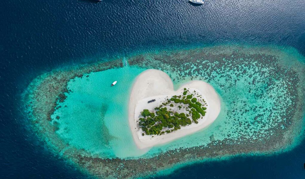 Aerial view of heart island in tropical Maldives, sandy island surrounded by corals and a few yachts, photo by Vitaliy Sokol, Depositphotos