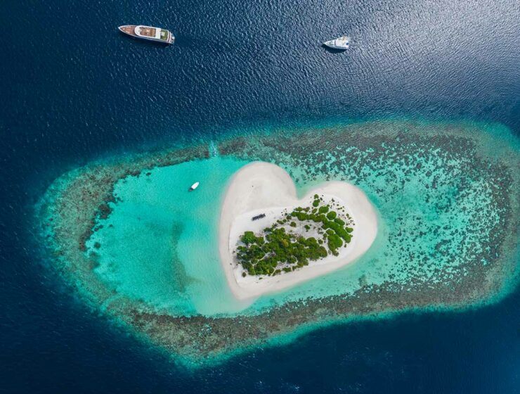 Aerial view of heart island in tropical Maldives, sandy island surrounded by corals and a few yachts, photo by Vitaliy Sokol, Depositphotos