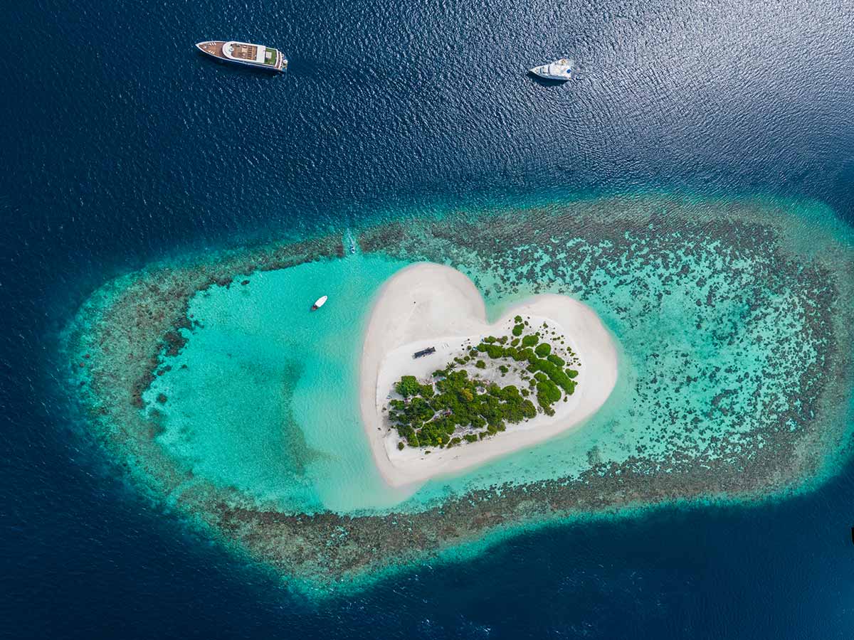 Aerial view of heart island in tropical Maldives, sandy island surrounded by corals and a few yachts, photo by Vitaliy Sokol, Depositphotos