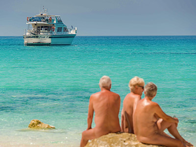 Naked people sitting on the beach in front of an anchored boat in Kefalonia island, Greece, photo by Vassaliki