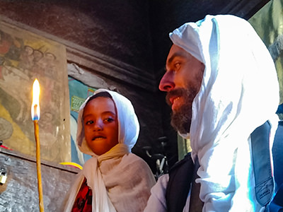 Five-year-old Ethiopian boy holding a candle, together with equally netela-covered Pipeaway blogger Ivan Kralj, on their return visit to Bete Giyorgis church in Lalibela, after a racial incident with Chinese photographers, Ethiopia, photo by Ivan Kralj