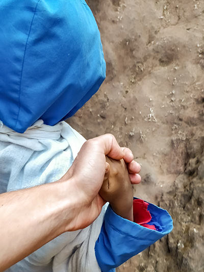 A five-year-old Ethiopian boy in blue hood holding a white hand of the photographer Ivan Kralj, while leading him through the trench out of the St. George Church in Lalibela, Ethiopia