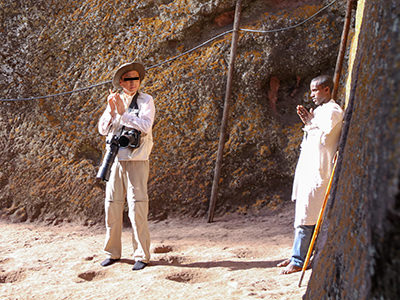 Sigey Melkame Bejena, a young Ethiopian, being instructed on how to hold palms in prayer for obsessive photography needs of an unnamed Chinese photographer with two large cameras around his neck, at Bete Giyorgis, a church in Lalibela, Ethiopia, photo by Ivan Kralj