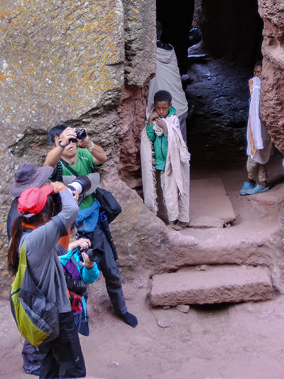 Ethiopian boys hiding behind netela scarf while Chinese photographers take their shots at Bete Giyorgis, a church in Lalibela, Ethiopia, photo by Ivan Kralj