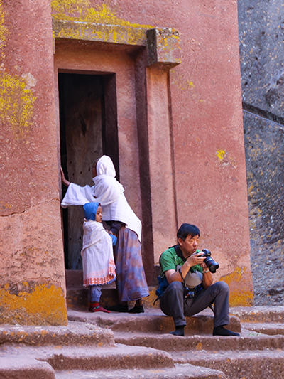 A boy in blue hood with his mother, looking at Chinese photographers sitting in front of the entrance to Bete Giyorgis church and looking in his camera, Lalibela, Ethiopia, photo by Ivan Kralj