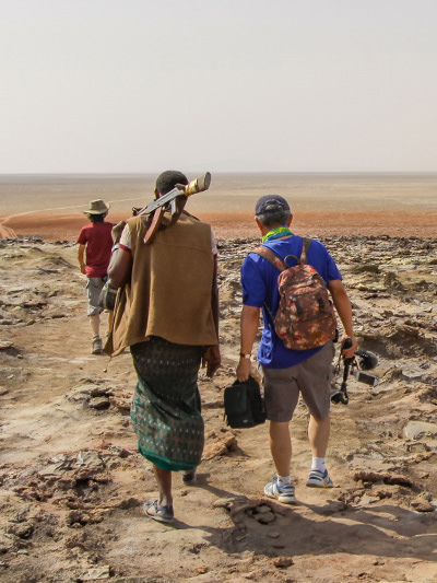 In the Afar Depression, a Chinese tourist with a selfie stick is escorted by a rifle-equipped Ethiopian security, Danakil Desert, Ethiopia, photo by Ivan Kralj