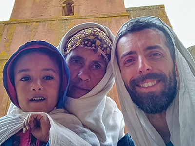 All covered with netelas, five-year-old Ethiopian boy Ashenafi Sisay, his mother Mame Esayte Woldemariam, and teary-eyed Pipeaway blogger Ivan Kralj posing for a photograph in front of Bete Giyorgis, the rock-hewn church in Lalibela, Ethiopia, after the incident conflict with Chinese tourists who were obsessively photographing churchgoers before being called out, photo by Ivan Kralj