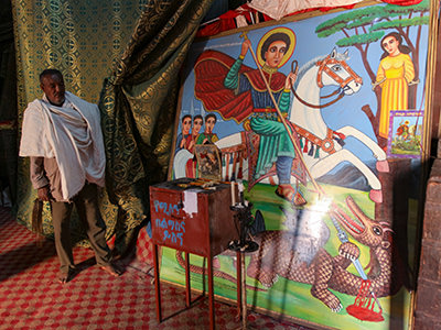 Church guardian at Bete Giyorgis church in Lalibela, Ethiopia, revealing the painting of Saint George killing the dragon hidden behind the curtain, photo by Ivan Kralj