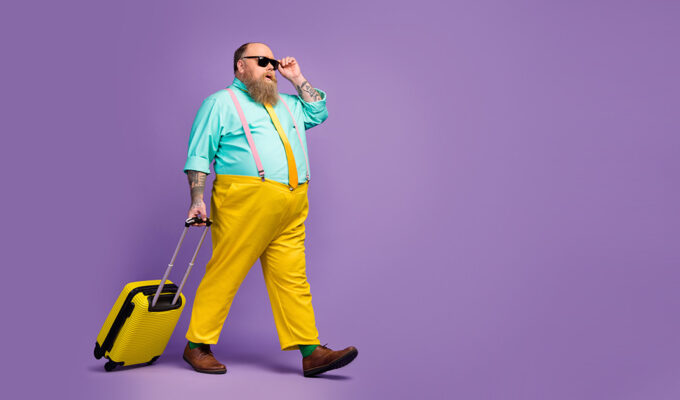 Colorfully dressed obese passenger in sunglasses walking to his plane with a wheeled yellow bag, photo by deagreez1, Depositphotos