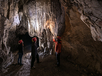 Visitors with helmets and flashlights under the stalactites of the Cave under Predjama Castle, credit: Postojna Cave Park, Slovenia.