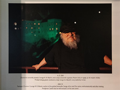 The photograph of George R. R. Martin during his visit to Predjama Castle in Slovenia, displayed in the lobby of Hotel Jama in Postojna.