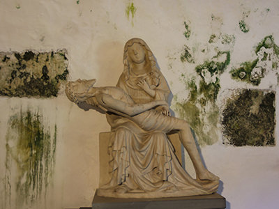 Pieta sculpture of Mary holding dead Jesus in front of a moldy wall in Predjama Castle, Slovenia, photo by Ivan Kralj.