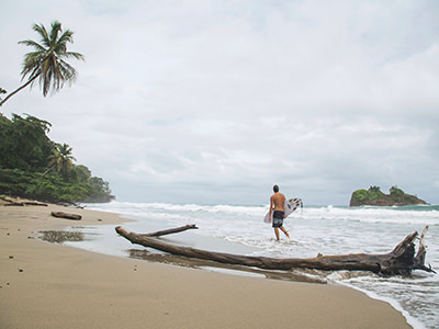 Surfer exiting the foamy water on a sandy beach in Puerto Viejo de Talamanca, Costa Rica, photo by Milada Vigerova, Unsplash.com.