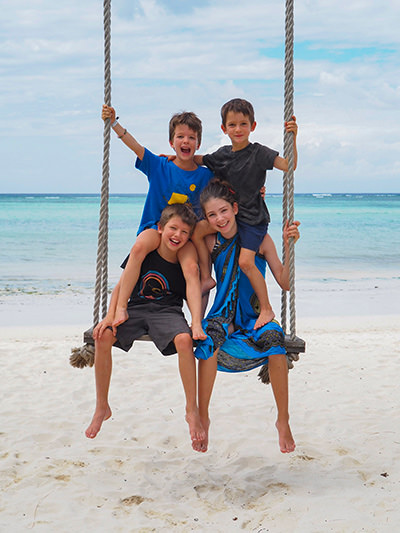 Edith Lemay's children posing in a swing on the white sand beach, during their world trip before three of them go blind, photo by Edith Lemay