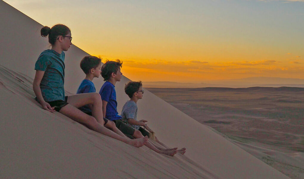 Lemay-Pelletier family's children gazing into distance while seated on a sand dune, on a world trip before losing they lose their eyesight due to retinitis pigmentosa genetic disorder, photo credit Edith Lemay