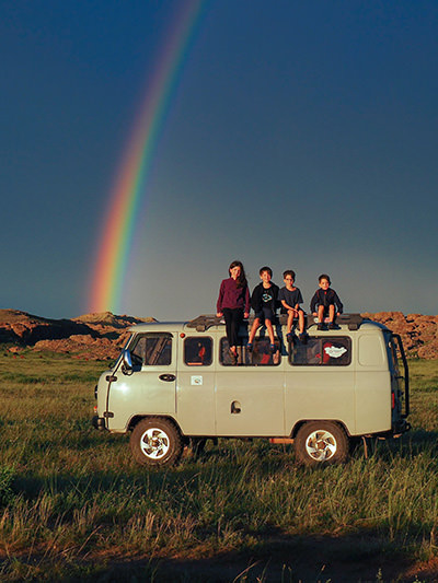 Edith Lemay's children sitting on a top of a minivan in Mongolia, with rainbow in a background, on their world voyage before they lose their vision, photo by Edith Lemay