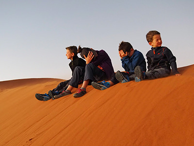Leo with his two brothers and a sister that have sensitive eyes due to retinitis pigmentosa, a genetic disorder that will eventually make them blind; four children are sitting on the sand dune in Namibia, covering their eyes from bright sunrise light and flying sand, during their world trip to fill their visual memory, photo credit Edith Lemay.