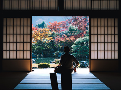 Person sitting in Tenryu-ji temple in Kyoto-shi, Japan, looking outside, at colorful vegetation, photo by Masaaki Komori, Unsplash.com.