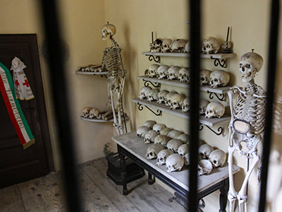 Human skeletons and skulls displayed in a chamber of the Ossuary of Solferino, with Italian flag and Red Cross insignia, photo by Ivan Kralj.