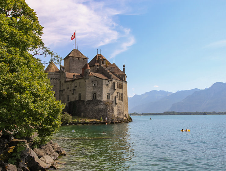 Exterior of Chillon Castle, island castle in Lake Geneva, with people swimming in its vicinity, photo by Ivan Kralj.