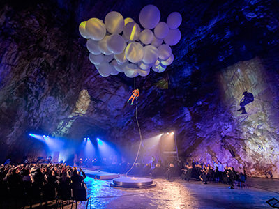 Man hanging from balloons in the Concert Hall of Postojnska jama, during the celebration of 200 years of cave tourism, copyright Postojna Cave Park Slovenia..