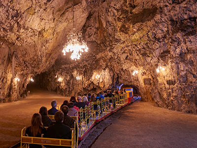 Electric train passing under a giant Murano glass chandelier in the Ballroom, the so-called dance hall of Postojna Cave, copyright Postojna Cave Park Slovenia.