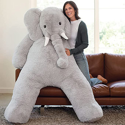 Woman on a sofa with a giant, 72-inch tall stuffed elephant, product by Vermont Teddy Bear.