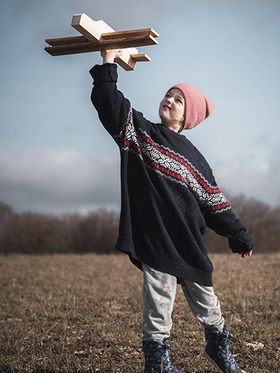 A girl playing with a plane toy in the field, photo by James Kovin, Unsplash.
