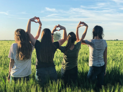 Girlfriends standing in a wheat field in Mexico, forming shapes of hearts with their fingers, photo by Melissa Askew, Unsplash.