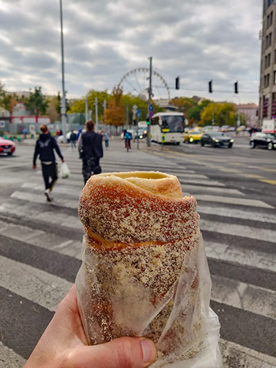 Kurtoskalacs or chimney cake, one of the best Hungarian desserts in Budapest, eaten as street food snack, with Budapest Eye ferris wheel in the background, photo by Ivan Kralj.