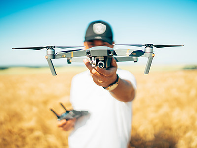 Drone pilot in blurred background, holding a Mavic drone in front in focus, photo by David Henrichs, Unsplash.