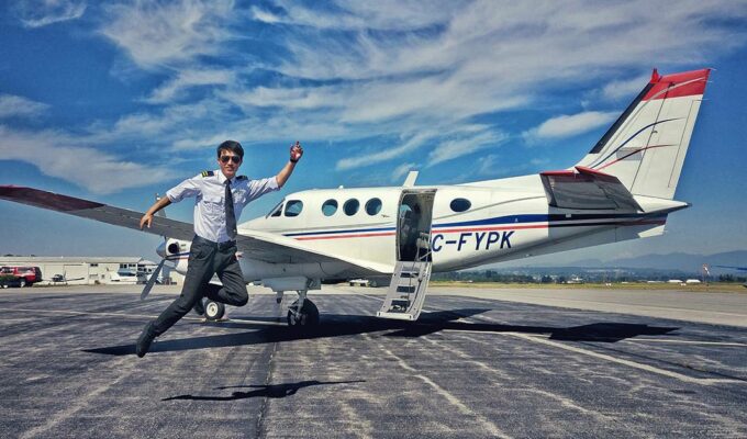 A pilot jumping in front of a parked airplane at an airport, photo by Kora Xian, Unsplash.