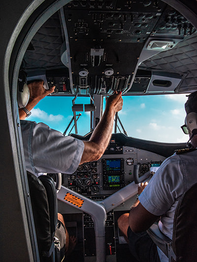Pilot and co-pilot operating a plane as seen through the cockpit door, photo by Rayyu Maldives, Unsplash.