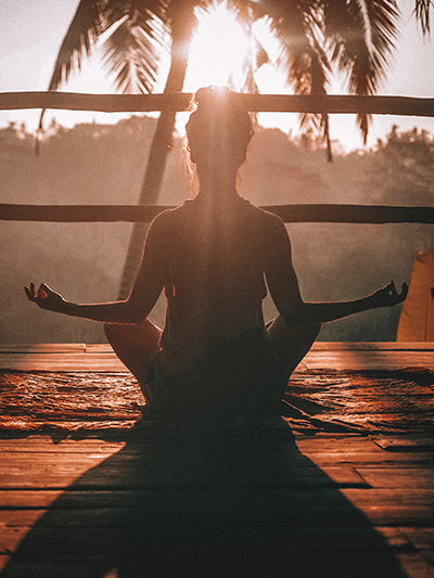 Woman in lotus pose, doing yoga in Ubud, Bali, Indonesia, in the backlight of the sun, photo by Jared Rice, Unsplash.