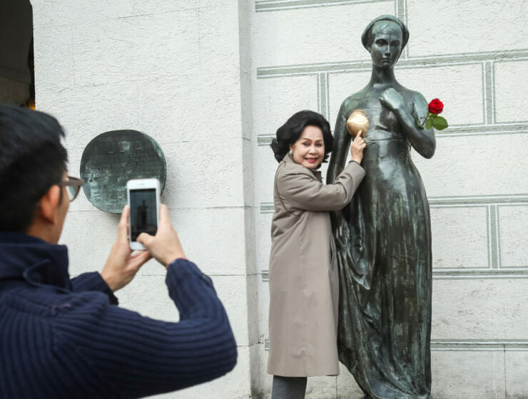 A woman posing for a photo standing next to the Juliet's statue in Munich, whose breast has changed color due to excessive statue rubbing by tourists, photo by Goran Jakus, Depositphotos.