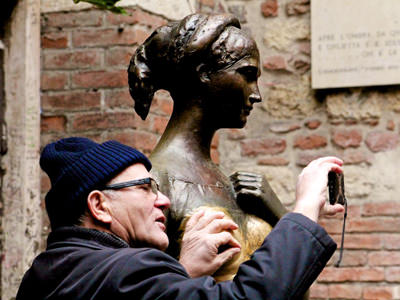 Older man taking a selfie with Juliet's statue in verona, while fondling her nipple; the excessive rubbing of the statue's breast, by the people believing it would bring them luck in love life, caused damage on the monument, photo by IkeofSpain.