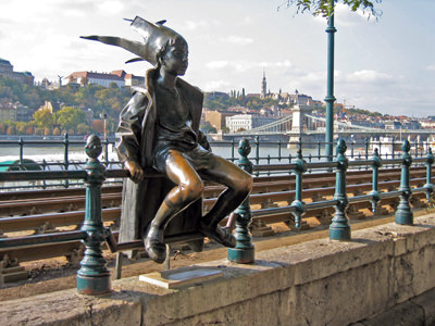 The statue of Kiskirálylány or the Little Princess, with makeshift crown, sitting on the tram railings in Budapest. Local belief says that rubbing the statuette's knees can secure good luck; photo by NH53. 