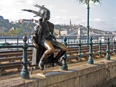 The statue of Kiskirálylány or the Little Princess, with makeshift crown, sitting on the tram railings in Budapest. Local belief says that rubbing the statuette's knees can secure good luck; photo by NH53.