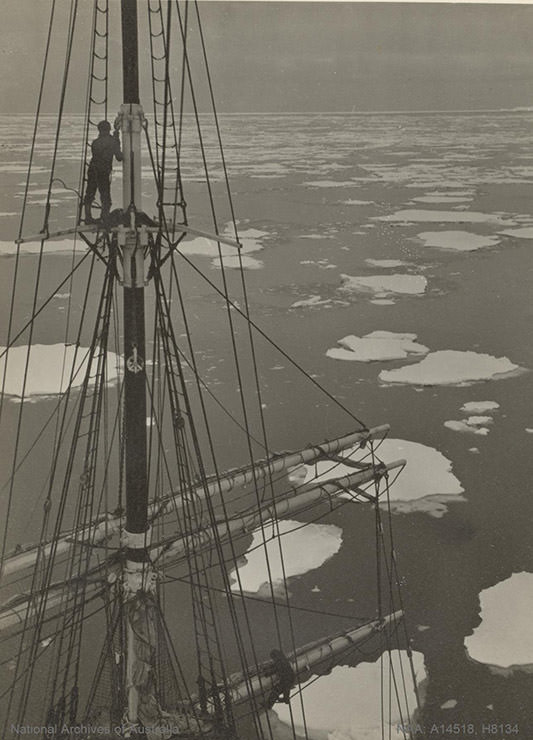 Man on mast of Discovery ship with loose pack ice ahead, somewhere in Antarctica, shot during the BANZARE expedition 1929-1931.