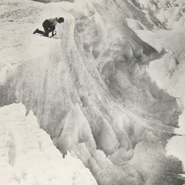 Man quarrying ice with a pick on the top of an ice cliff, shot during the Australian Antarctic Expedition 1911-1914.