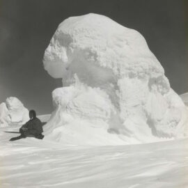 Man sitting next to the ice hill in Antarctica, sometimes between 1901 and 1936.
