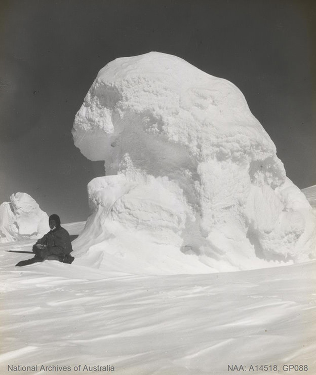 Man sitting next to the ice hill in Antarctica, sometimes between 1901 and 1936.