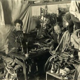Men sewing on the sewing machine and cutting rope in the cabin during the British Antarctic Expedition 1907-1909.