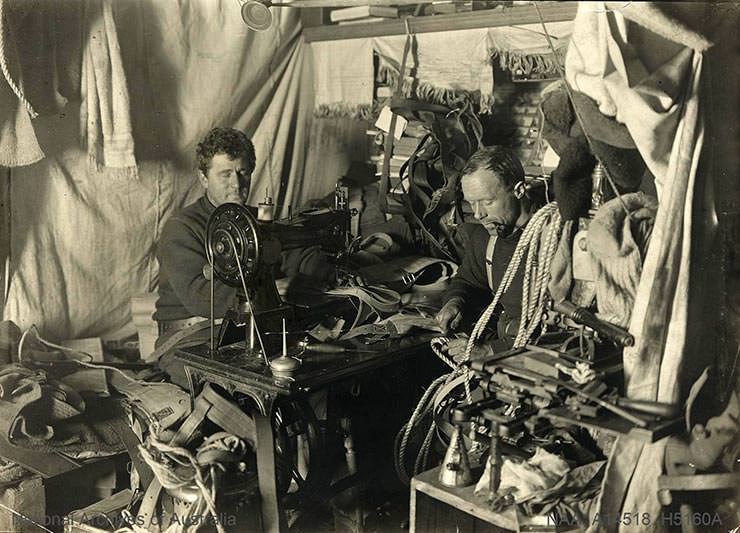 Men sewing on the sewing machine and cutting rope in the cabin during the British Antarctic Expedition 1907-1909.