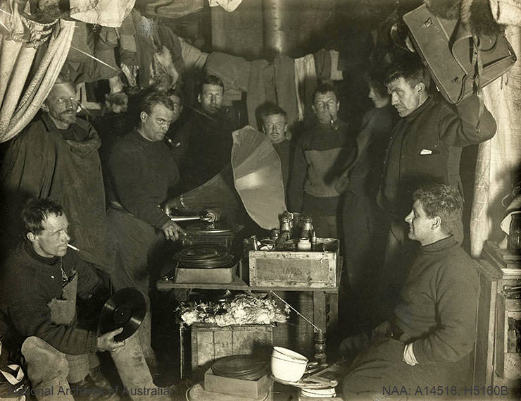 Antarctica explorers standing around a large gramophone in their hut, during the British Antarctic Expedition 1907-1909.