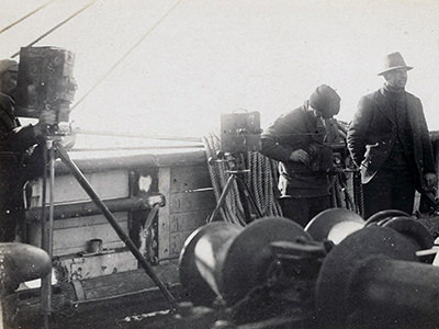 Men taking photographs aboard a ship during an unknown Antarctic expedition, copyright National Archives of Australia.