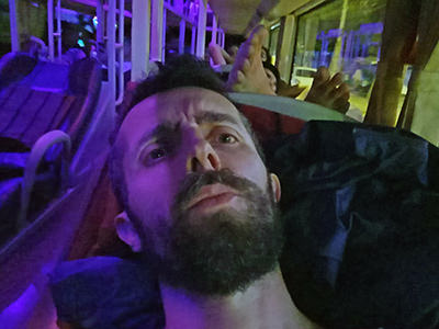 Travel blogger Ivan Kralj sitting in a sleeper bus to Hoi An, Vietnam, while passenger behind him is resting his feet on the headrest; photo by Ivan Kralj.