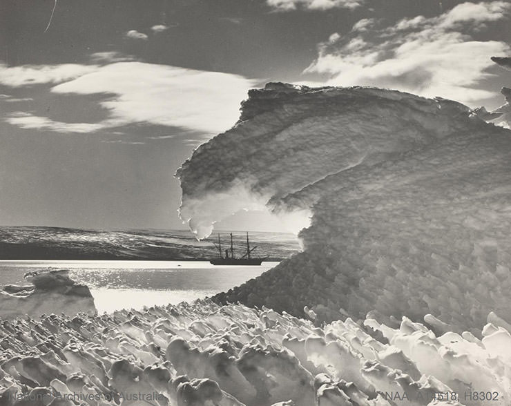Tumbling ice wave with sea and ship in distance, shot during the Australian Antarctic Expedition 1911-1914.