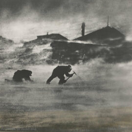 Two men quarrying ice with picks during a strong blizzard in front of their living huts in Antarctica, shot during the Australian Antarctic Expedition 1911-1914.